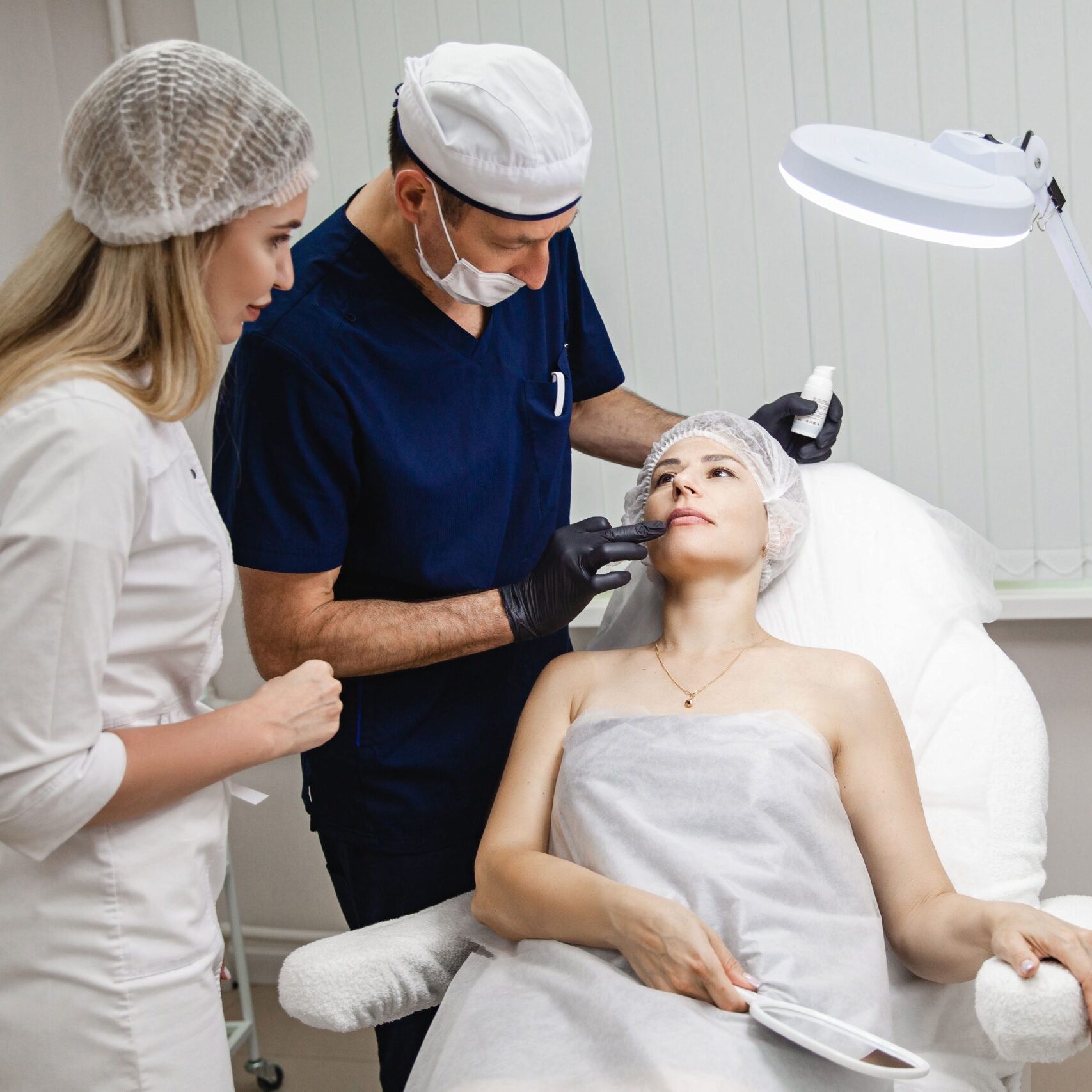 A man doctor together with a girl assistant examine the patient's woman before a lip augmentation procedure in a cosmetology clinic. High quality photo